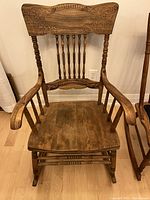 Front view of the wooden oak rocking chair showing carved backrest, spindles, arms, and smooth seat.