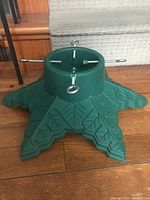 Side angle view of the green plastic Christmas tree stand showing its star-shaped base and three of the four metal tightening screws with eyelets.