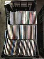Photo showing a black plastic crate filled with three layers of CD jewel cases.
