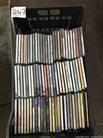 Top view of a black crate filled with roughly 48 used CD jewel cases lined up in rows.
