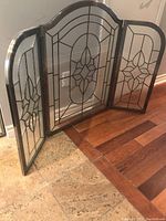 Full view of the three-panel fireplace screen standing on a floor showing decorative glass with metal designs and metal frame.