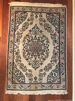 Full image of rectangular hand woven wool and silk rug with central medallion floral design and fringed edges.