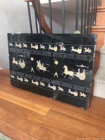 Full view of the large rectangular lacquered wall panel standing upright, showing the complete Oriental design with chariots and horses.