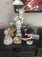 Group of assorted collectible porcelain figurines including lady with umbrella, girl figurine, small cottage, and statuette of a person with ball