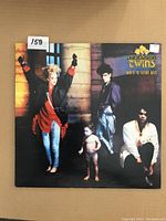 Front cover of Thompson Twins LP album 'Here's To Future Days' showing band members with a child and architectural background.