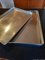 Two aluminium sheet pans stacked, showing the rolled edges and overall condition.