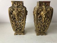 Front view showing the pair of antique brass vases with detailed gothic filigree and sculpted faces.