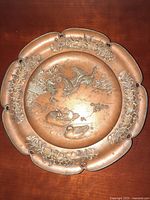Front view of antique bronze plate showing embossed birds, fish, and floral garlands on scalloped edge