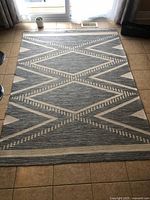 Gray and cream geometric area rug laid flat on tile floor showing full size and pattern.