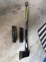 Image showing a 36-inch axe with a black and yellow handle lying on the ground next to two smaller black metal wood splitters.