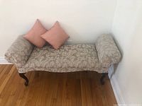 Bench viewed from the side showing floral upholstery, armrest, and one pink cushion on the bench seat.