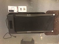 Photo showing black Bigzzia treadmill with walking belt, power cord, and manual on floor surface.