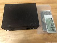 Closed black metal box on wood surface with plastic bag of banknotes beside it