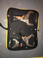 Three locking C-clamps of different sizes secured inside a black and yellow carrying case, showing the clamps with orange trigger locks and metal bodies.