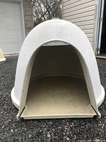 Front view of the white dome-shaped Dogloo dog house showing open entrance and removable floor panel extended outward.