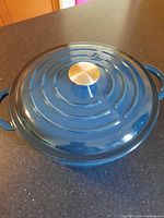 Blue enamel Dutch oven with lid, showing top view with metallic knob and concentric ring design on lid.