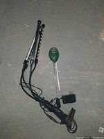 Three LED grow light bars with clips, all attached to cables with a power adapter, and green soil moisture meter with two prongs placed on a floor.
