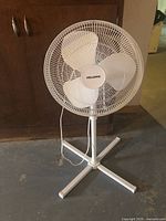 White Pelonis pedestal fan with protective grille, three clear blades and cross-shaped base