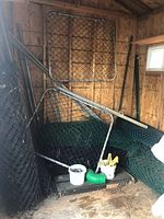 Fencing rolls, metal gate frames, bucket with fittings and accessories inside a wooden shed.