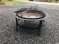 Firepit angled view showing legs, mesh dome cover, and rusty fire bowl.