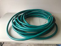 Photo of a green, coiled 50 foot garden hose laid on a white surface.