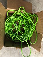 Bright green electrical extension cord loosely coiled inside a cardboard box. The cord appears intact and in good used condition.