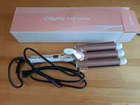 Ohuhu 3 barrel hair curler wand next to its box showing the styling tool and power cord.