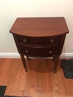 Front view of wooden hallway table showing two curved drawers with brass round handles and keyholes.