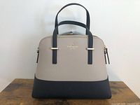 Front view of two-tone dome satchel handbag on wooden surface