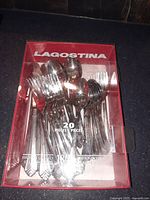 Top view of a boxed set of Lagostina cutlery showing forks, spoons, and knives arranged inside on a plastic holder, box labeled 20 pieces.