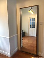 Large full-length mirror with medium-tone wooden frame reflecting room interior