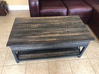 Rectangular lift-top coffee table, top closed, wood-look laminate finish, black metal frame, lower shelf visible