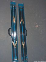 Two blue foldable saw horses folded flat showing black carrying handles and brass colored locking hardware on top view.