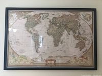 Framed National Geographic world map showing detailed political and geographical information in vintage style, with inset globes and muted colors.