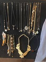 Full view of jewelry lot including necklaces and bracelets against black background, arranged hanging and laid out