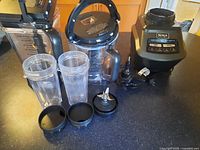 Full view of kit components including blender base, food processor bowl, two 2-cup blending cups with lids, and blade attachments laid on countertop.