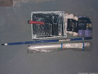 Paint trays with metal grid inserts, paint rollers (some used, some new), roller extension pole, and large roll of clear masking film