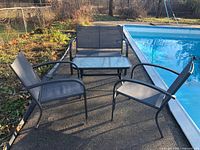 Full view of patio set including glass table, loveseat, and two chairs near pool and garden area.