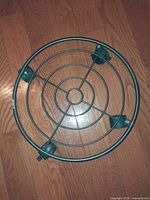 Photo of a circular metal plant wheel with four rollers on a wood floor.