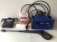 Photo showing entire pressure washer set with unit, spray gun, wand, detergent container, and mount holder all placed on a flat surface, black hose coiled behind the unit.
