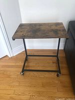 Side table front view showing wooden top and metal frame with wheels on hardwood floor.