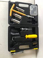 Open black plastic carrying case showing spark plug replacement tools including sockets, wrenches, brush, and accessories.