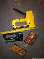 Photo of two staplers and three packs of staples on concrete floor. The yellow Stanley heavy-duty stapler is on top, black Bostitch staple gun below, along with staple packs.