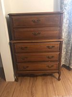 Front view showing the dresser's 5 drawers with decorative metal handles, brown finish, and carved legs.