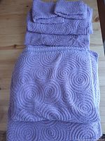 Photo showing the entire towel set stacked on a wooden surface with visible circular swirl pattern and purple color.