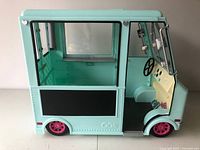 Side view of the mint green toy food truck showing the large serving window with a black panel, pink wheels, and empty interior.