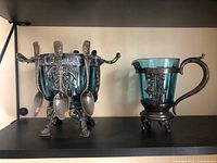 Front view of sugar bowl with four spoons and matching blue glass cup on shelf