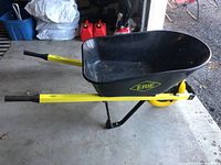 Side view of the Erie wheelbarrow showing yellow handles, black plastic tray, single wheel and metal support frame.