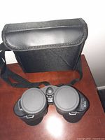 Top-down view of WholeV binoculars with lens covers on and carrying case behind