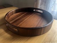 Angled side view of a thick round wooden serving tray with cut-out handles